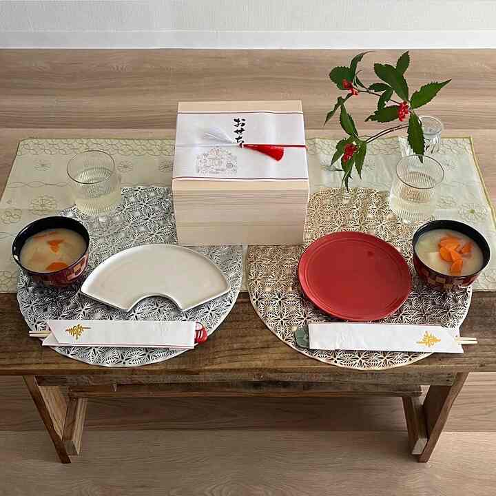 明るい木の床の上に配置された伝統的な和風お正月のテーブルセッティング、テーブルランナーと丸いランチョンマット、皿と汁椀が調和したインテリア