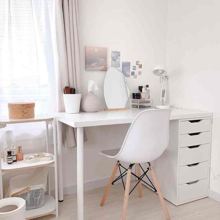 White-toned home office featuring a simple desk and chair with a mirror and makeup items creating a clean workspace