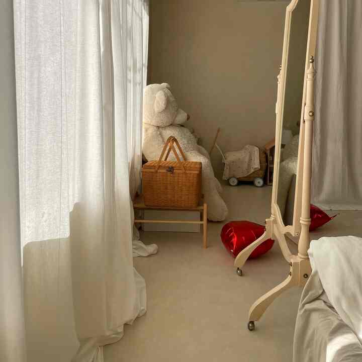 Natural-toned kids' room featuring a large teddy bear, woven basket, and standing mirror with cozy atmosphere