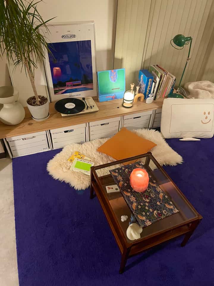 深い紫色のラグが敷かれたリビング、木製の棚とクッション、コーヒーテーブルが落ち着いた雰囲気を演出