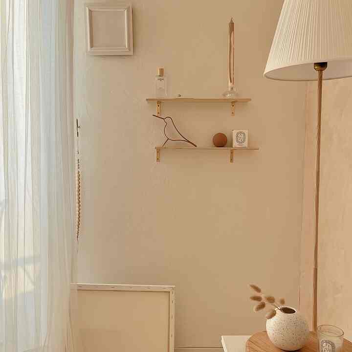 暖かいベージュの自然な色調の壁にシンプルな木製棚とフロアランプが配置された、落ち着いた北欧風のインテリア