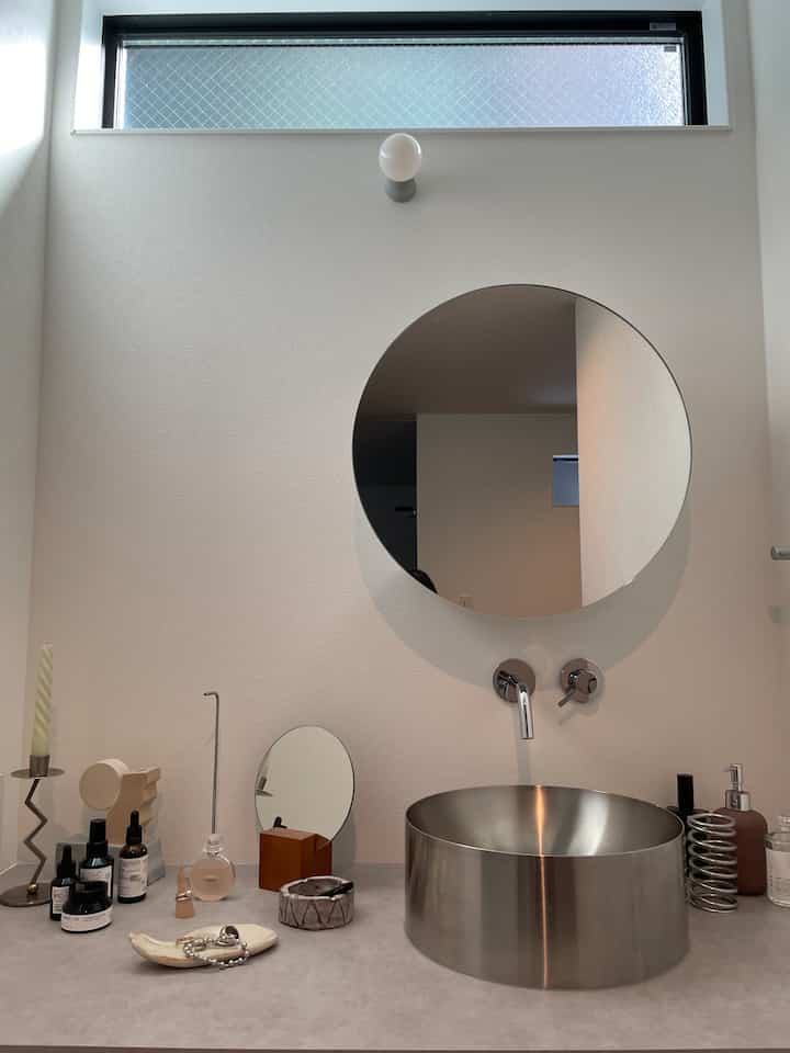 白を基調とした壁とメタリックなスピニング洗面器、丸い鏡が配置されたシンプルな雰囲気のバスルーム