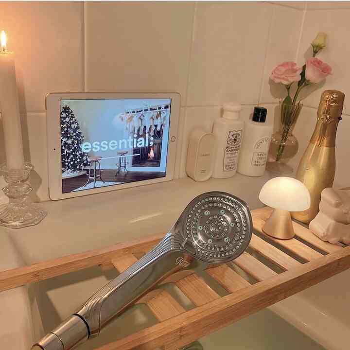 白いタイルのバスルーム、木製のバスラックにシャワーヘッド、キャンドル、花瓶、小さなランプが置かれた雰囲気のある空間