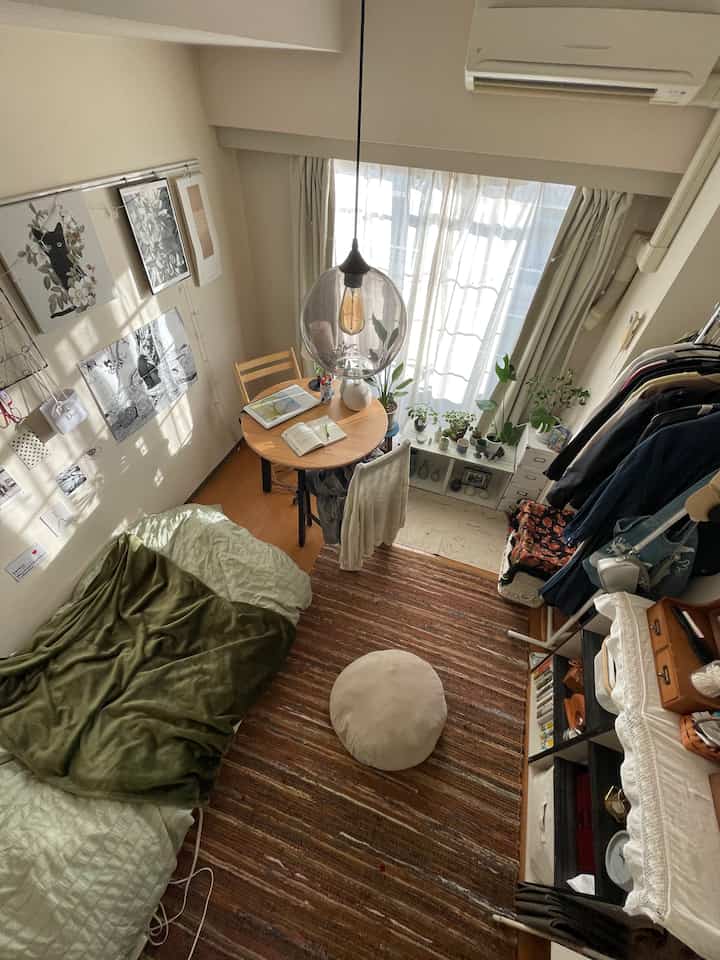 Natural-toned studio apartment living room featuring a sofa bed, round dining table, and large rug creating a cozy atmosphere
