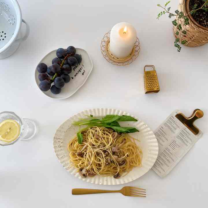 白を基調としたダイニング、白いテーブルクロスの上にパスタ皿、ブドウ、キャンドル、植物が配置されたシンプルで印象的な空間