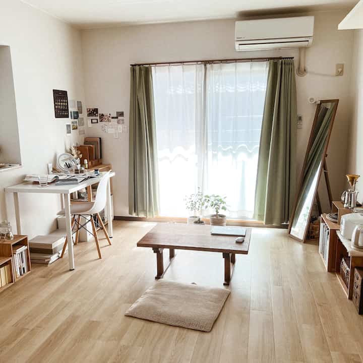 Beige and wood tone single household living space featuring natural light and simple furniture layout with a cozy home office atmosphere