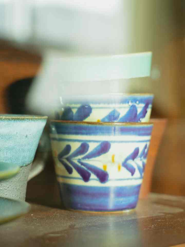 ナチュラルカラーの空間に配置された英国ヴィンテージのキャビネットに青い模様の陶器皿とボウルが収納されている印象的なインテリア