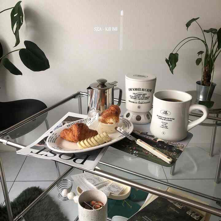 透明なガラステーブルにクロワッサンとコーヒー、白いマグカップが配置されたナチュラルモダンなホームカフェ空間