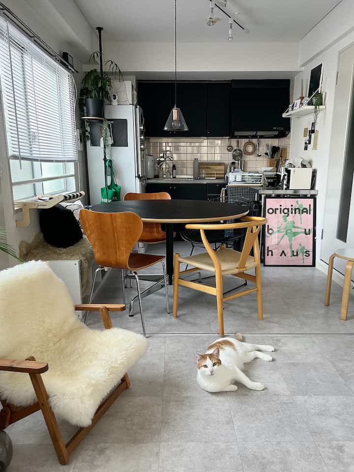 A white and black tone kitchen and dining room featuring wooden chairs, a cozy armchair, and a cat lying on the floor