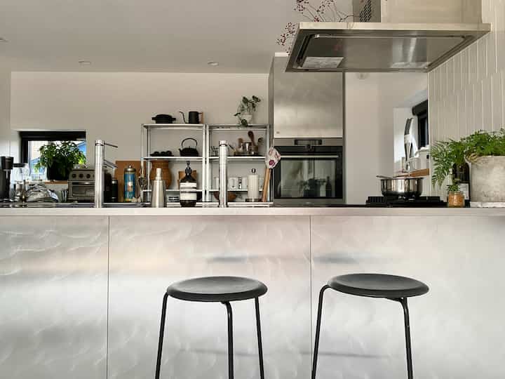 Modern kitchen in white and stainless steel tones featuring counter with bar stools and open shelving