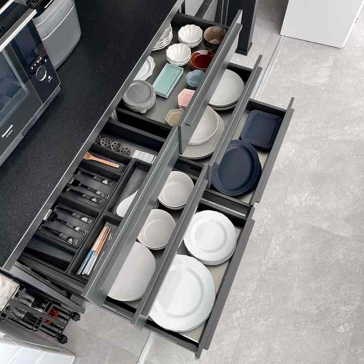 黒い調理台ときれいに整理されたキッチンの引き出しに、様々な色の皿と調理器具が配置されたモダンなキッチン空間