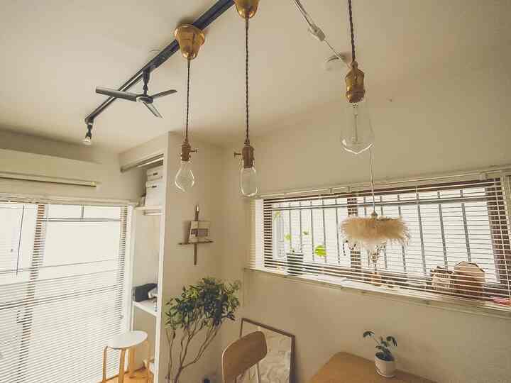 白とゴールドの色調のダイニングルーム、ペンダントライトとスツール、植物が配置されたナチュラルな雰囲気のインテリア