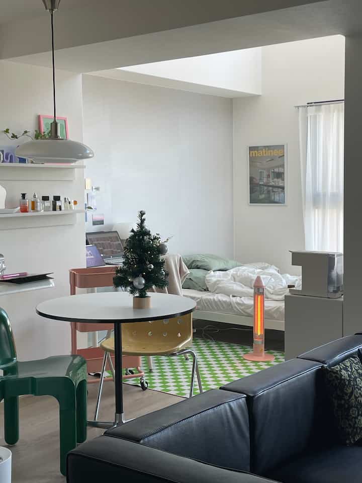 Bright white-tone studio apartment living and bedroom space featuring black leather sofa, round dining table, and bed with minimalist modern style