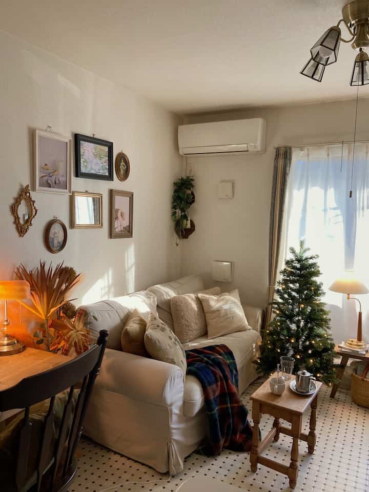 暖かいブラウンとホワイトのトーンのリビング、ホワイトのソファとクリスマスツリー、小さな木製テーブルが印象的な空間。