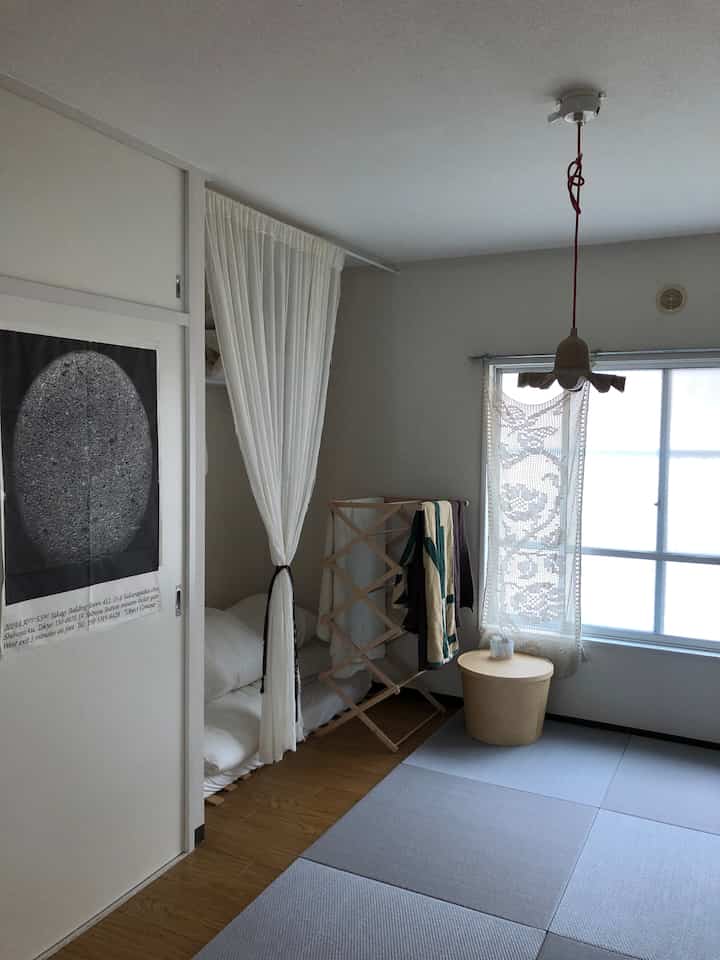 明るいホワイト調のコンパクトな部屋、中央に木製の物干しと小さな丸テーブルが配置されたナチュラルモダンなインテリア