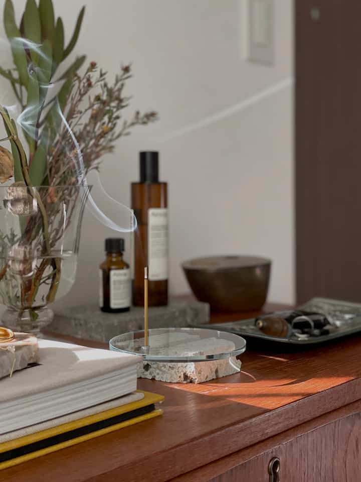 ナチュラルな色調の玄関、アロマの煙と植物の飾りが配置された木目調のテーブルがある落ち着いた雰囲気のインテリア