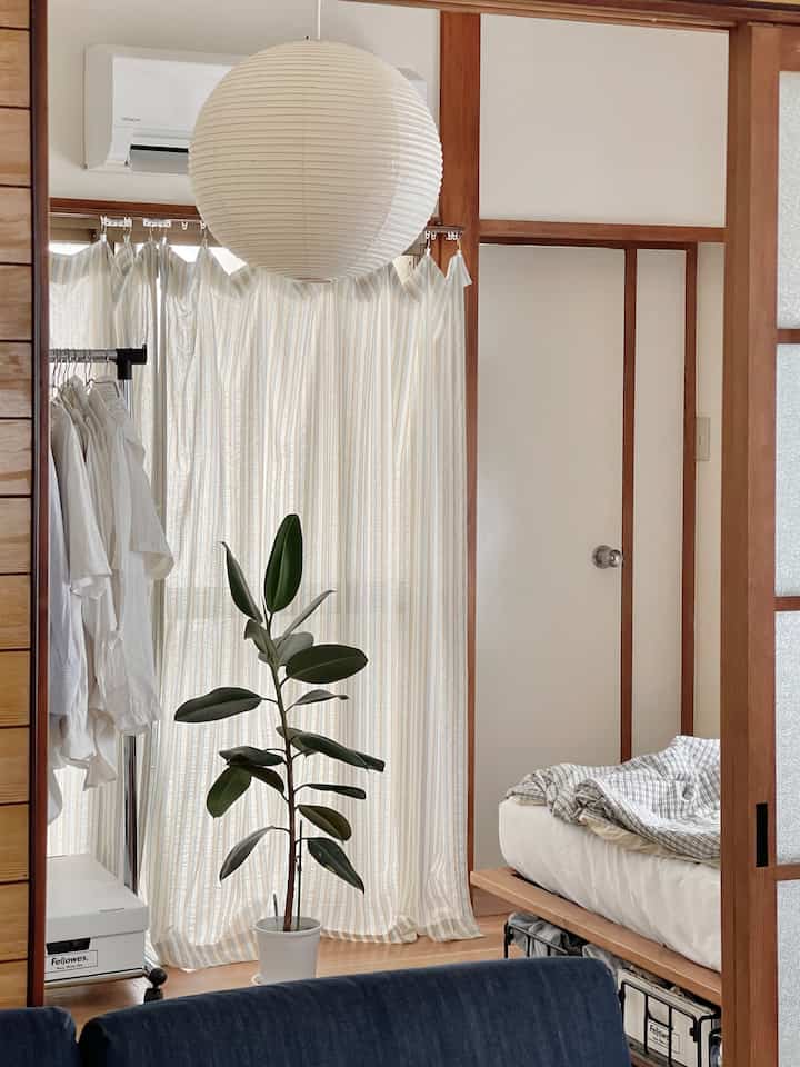 木目調とベージュのカーテンが調和したワンルーム寝室、デニムソファと観葉植物が配置された落ち着いた雰囲気のインテリア