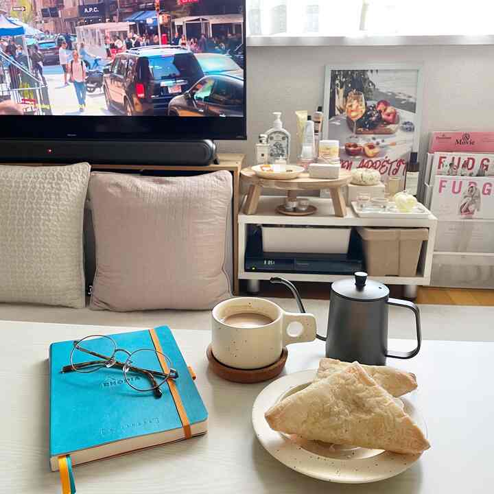 White and brown toned living room featuring sofa, TV, notebook, and coffee creating a cozy home cafe vibe