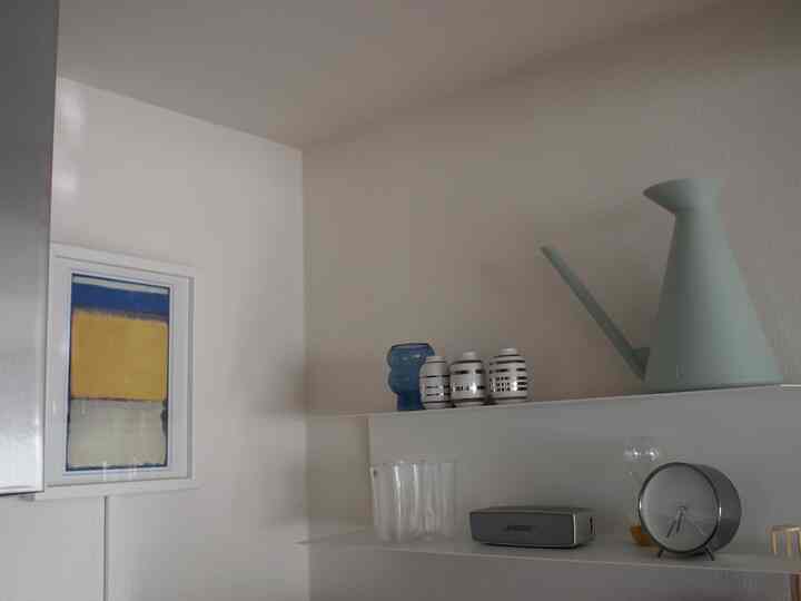 白い壁のキッチンに、青と黄色のポスターと飾りが配置されたミニマルで雰囲気のあるインテリア