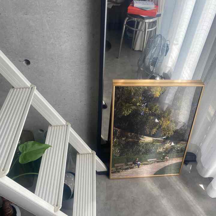 グレー基調の空間、ゴールドフレームのポスターとメタルスツールが配置されたモダンなインテリア