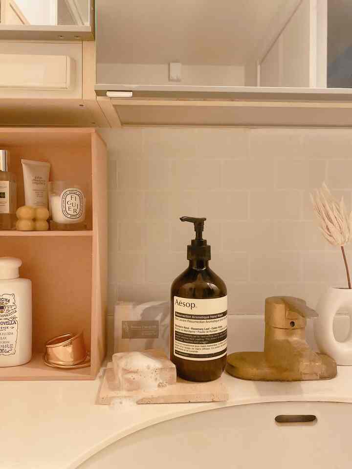 温かみのあるベージュと白の色調のバスルーム洗面台、ラタンのトレイとバスルーム用品が配置された落ち着いた空間