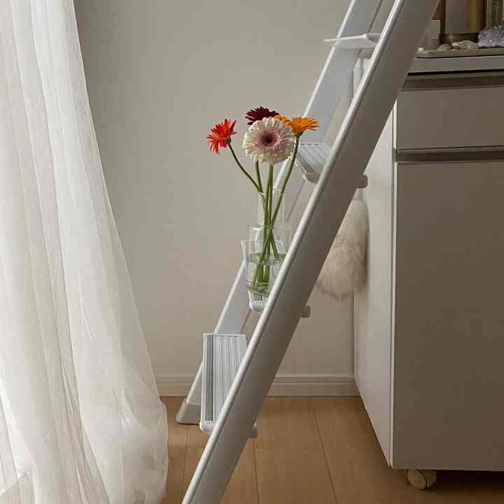 ホワイトと木目調のリビング、透明な花瓶にカラフルな花が飾られた梯子が配置された雰囲気のある空間