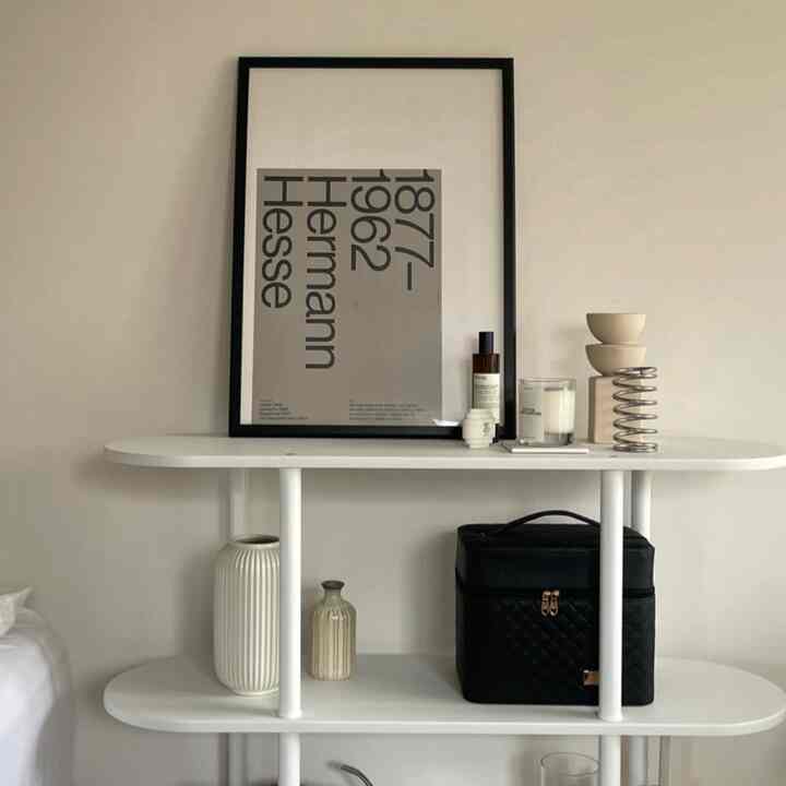 モノトーンの落ち着いた空間、白い棚にポスターや花瓶、装飾品が配置された印象的なインテリア