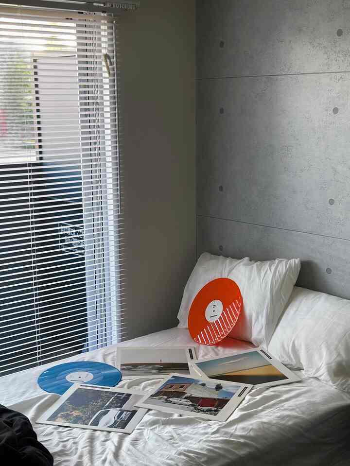 白とグレーのトーンの寝室、白い寝具の上に青とオレンジのレコードが置かれたミニマルでモダンな印象的な空間