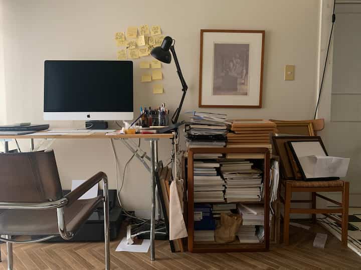 ホワイトとナチュラルトーンのホームオフィス、折りたたみデスクと多数の書籍、額縁が配置された落ち着いた作業空間