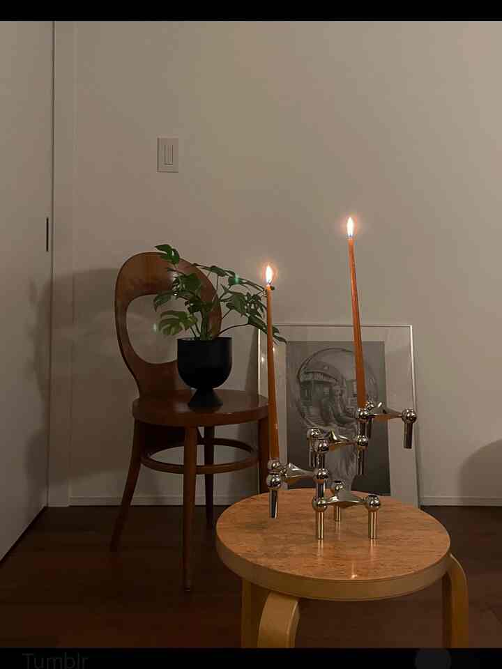Wood tone living room featuring a round-legged chair, potted plant, and lit tapered candles creating a simple and serene atmosphere