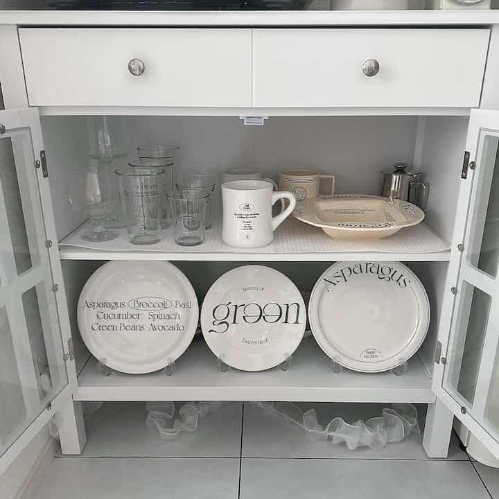 White tone kitchen dining cabinet interior featuring neatly arranged glasses, mugs, and plates in a clean space