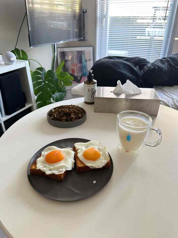 白と黒のトーンのワンルーム、白い丸テーブルに目玉焼きトーストとミルクのグラスが置かれた雰囲気のあるホームカフェ空間