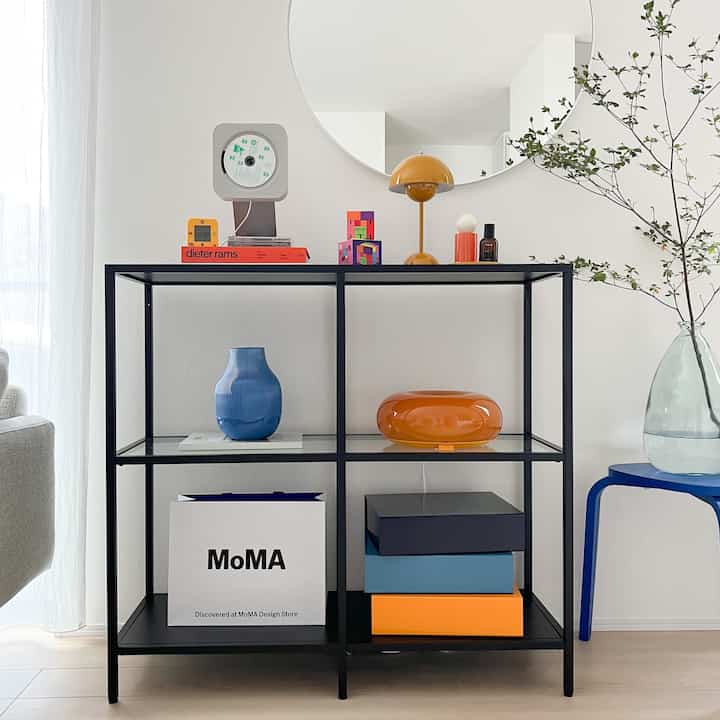 Modern living room with white walls and black metal shelf featuring an orange lamp and blue decorative vase, creating a clean look