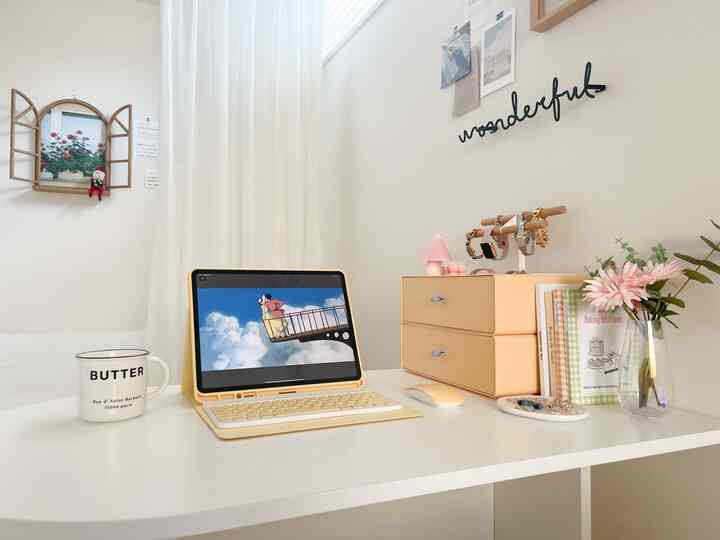 白と淡い黄色のトーンのホームオフィス、整ったデスクにタブレットや収納引き出し、小物トレイが配置されたきれいな雰囲気のインテリア