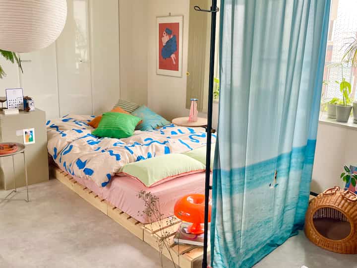 白と青のトーンの寝室、木製のベッドと多様なクッションが配置された雰囲気のあるインテリア