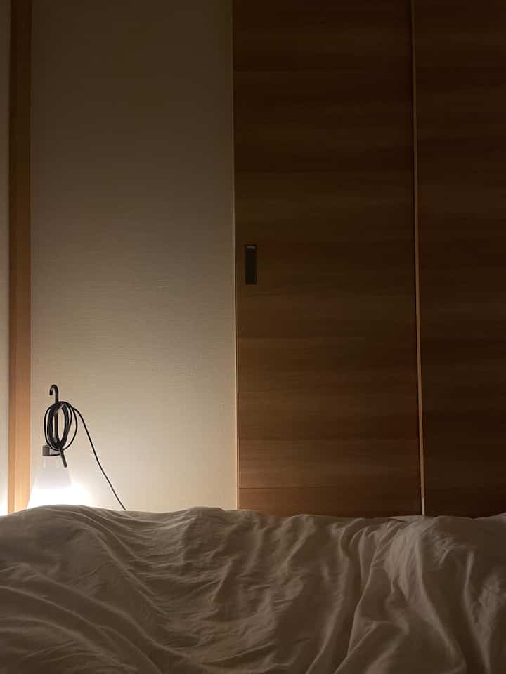 自然な色調の寝室、白い寝具と木製の引き戸、温かみのあるテーブルランプが配置された雰囲気の良いインテリア