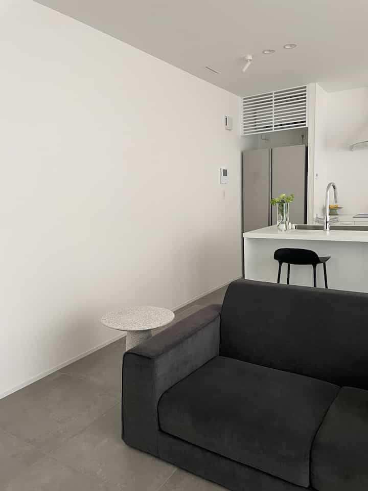 白とダークグレーのトーンのリビングとキッチン、ダークグレーのソファと小さなサイドテーブルが配置されたモダンなインテリア