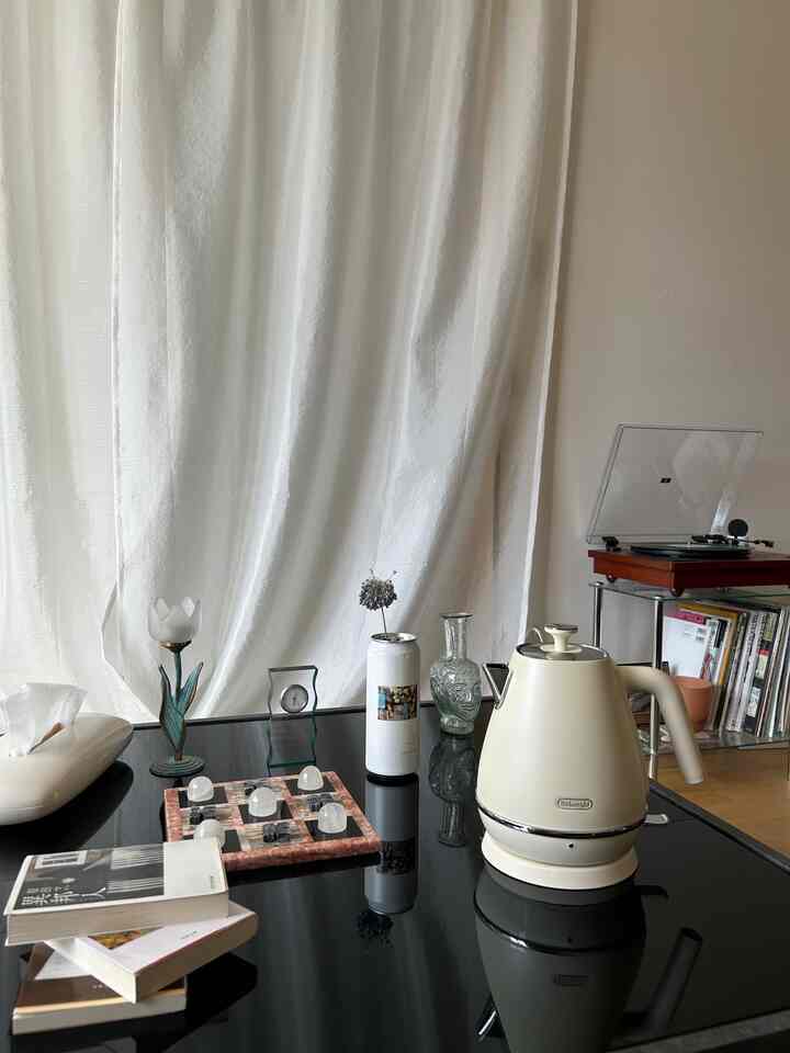 アイボリー色の電気ケトルとレコードプレーヤーが配置された黒いガラステーブルのある自然なキッチンスペース