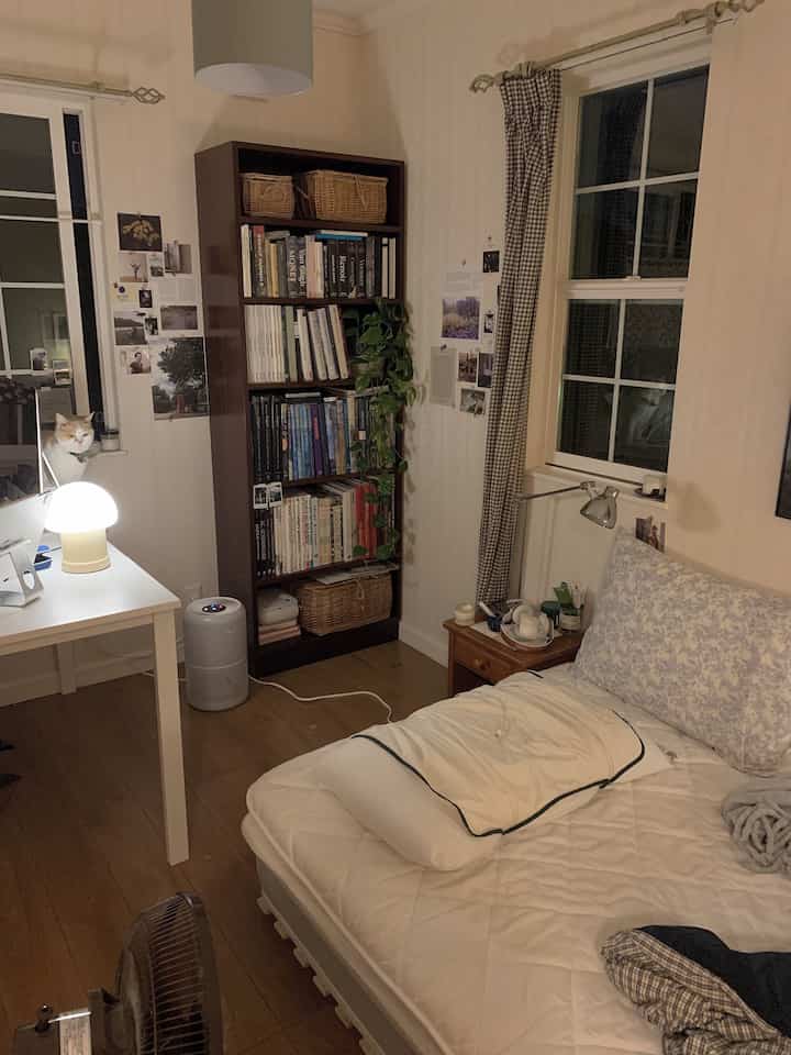 白と茶色のトーンの寝室、書棚とデスクが配置された印象的でコンパクトな空間