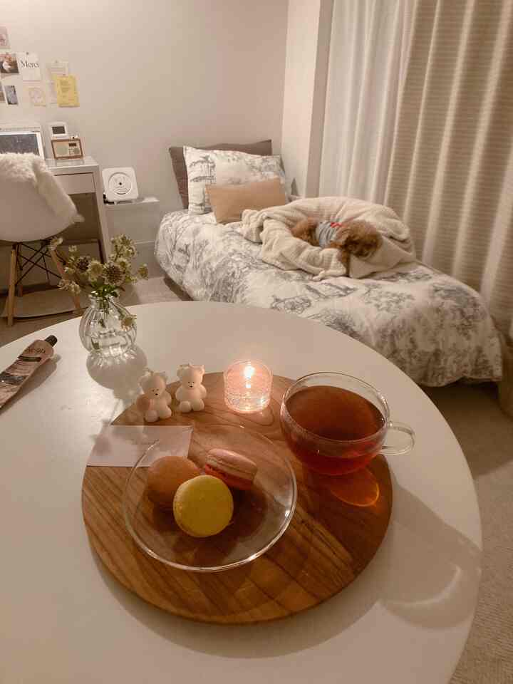 Warm white and brown toned bedroom featuring a dog on the bed, lit candles, macarons and tea on a table creating a cozy atmosphere