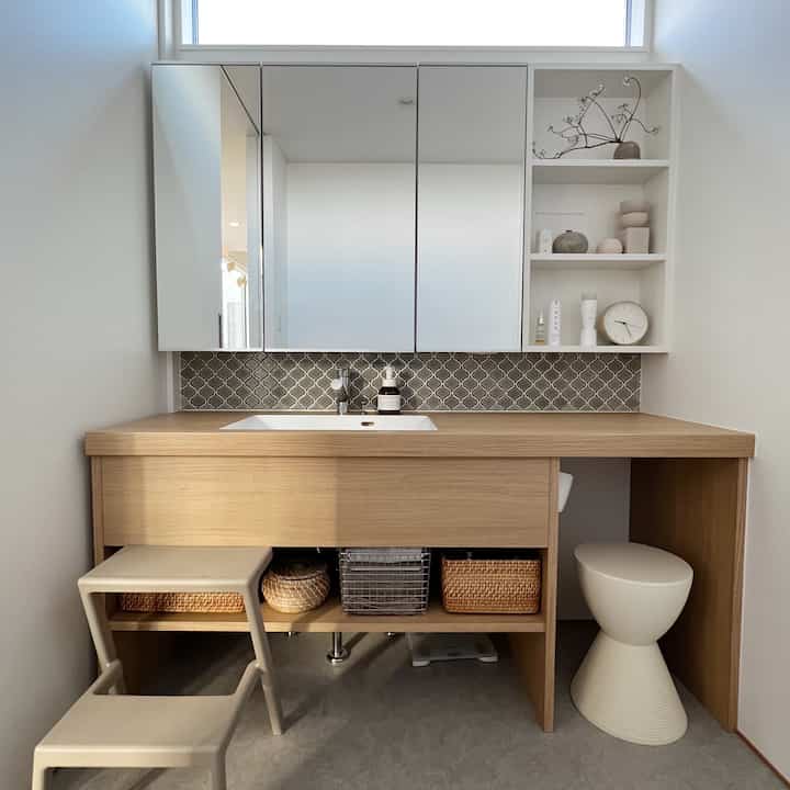 A modern powder room in white and wood tones featuring woven storage baskets and a stool in a clean layout