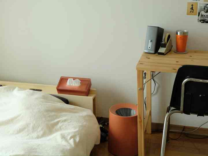 ナチュラルな木目調とシンプルなスタイルの寝室、左にベッドとティッシュケース、右にデスクとゴミ箱が配置された空間