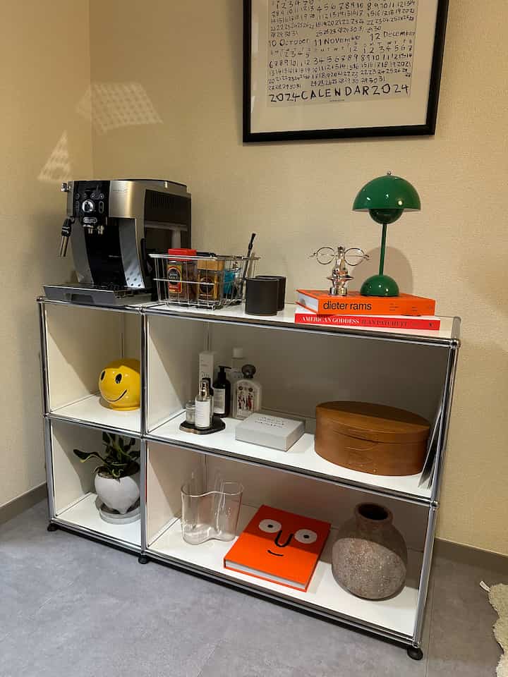 白いメタルキャビネットの上にデロンギのコーヒーメーカーと緑のランプ、本が配置されたミッドセンチュリーモダンなリビングインテリア