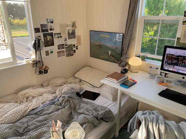 A modern home office and bedroom in white and beige tones featuring a bed, desk, and wall decor