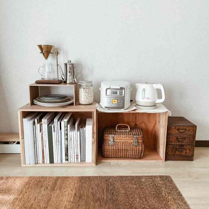 ナチュラルな木目調と白色の小さなリビング、木製収納ボックスに本や調理家電が整然と配置された雰囲気のあるインテリア