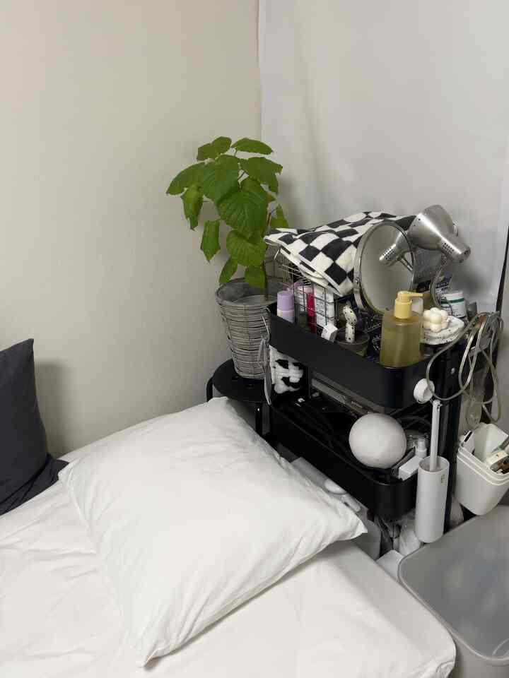 白と黒を基調とした寝室、化粧品収納カートと植物が配置された雰囲気のある小さな空間