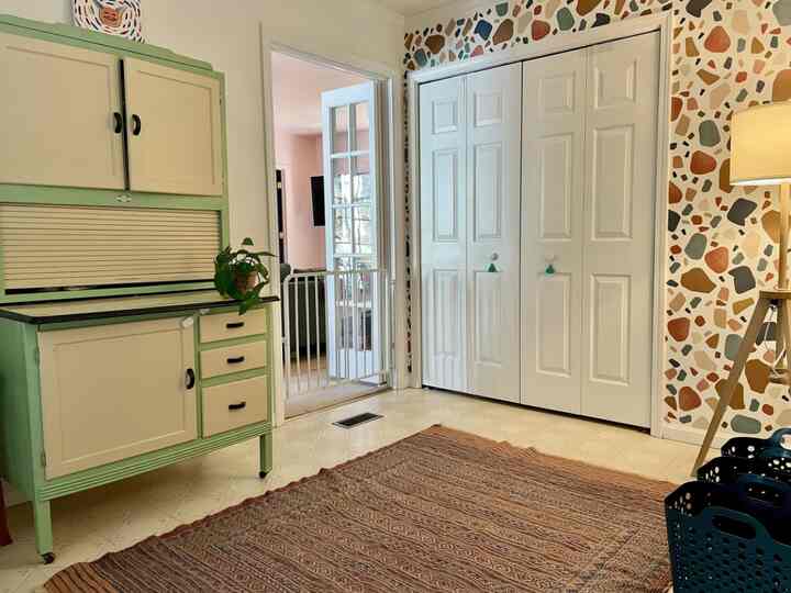 Bright and cozy hallway featuring beige-green vintage storage cabinet, white built-in closet, and colorful patterned wallpaper