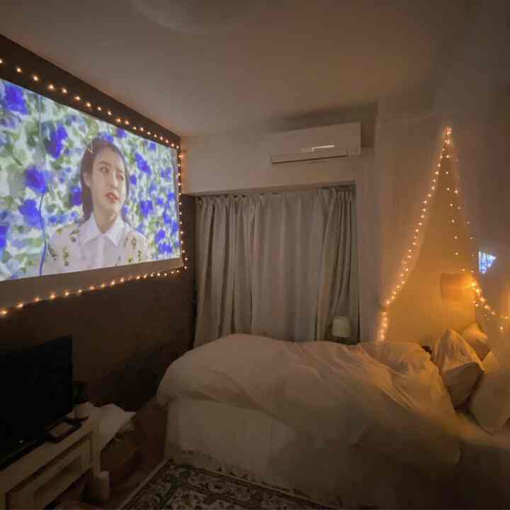 白とグレーのトーンの寝室、プロジェクター画面とストリングライトが配置された雰囲気のあるホームシネマ空間