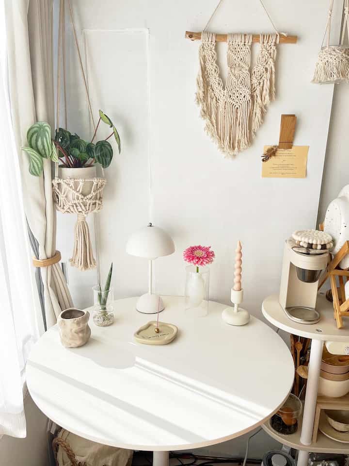 White and natural tone studio dining room featuring macrame wall hanging, plants, and cozy decor elements