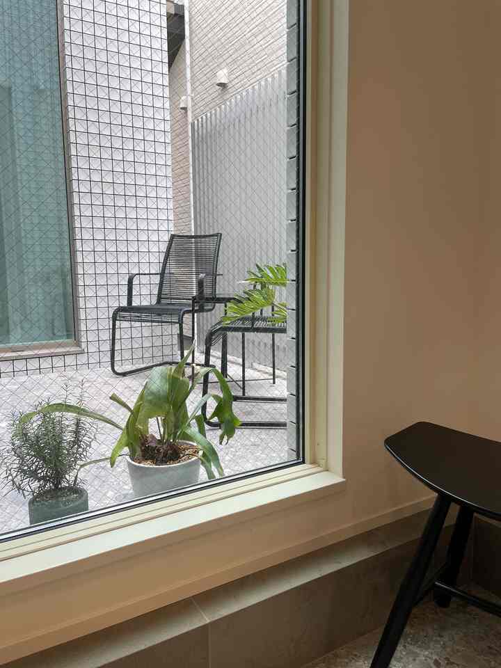 ベージュ調の玄関インテリア、窓越しにアウトドアチェアが見え、内部には黒色のスツールが配置された清潔感のある空間